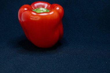 Canlı kırmızı bir dolma biber koyu mavi bir zemin üzerine oturmuş taze rengini ve pürüzsüz dokusunu sergiliyor..