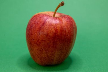 Taze, kahverengi saplı kırmızı bir elma, yeşil bir zeminde, sağlıklı bir aperatif veya teşhir için hazır bekliyor..
