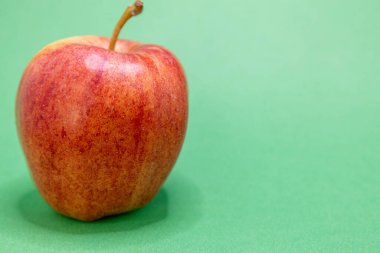 Canlı kırmızı ve sarı bir elma açık yeşil arka planda belirgin bir şekilde sergilenir ve tazeliğini vurgular..