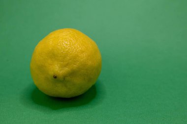 Parlak sarı bir limon zıt yeşil bir zemin üzerinde sergilenir, taze görünümünü vurgular..