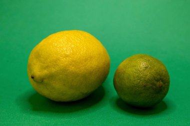 Parlak sarı bir limon ve yeşil bir kireç canlı yeşil bir yüzey üzerinde duruyor. Bu da turunçgillerdeki kontrastı gösteriyor..
