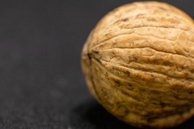 Tek bir cevizin detaylı makro çekimi, kabuğunun eşsiz, engebeli dokusunu karanlık bir zemine karşı sergiliyor..