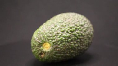 Avokadonun engebeli yeşil derisini ve benzersiz şeklini gösteren yakın plan görüntüsü. Işıklandırma, onun taze ve olgun görünümünü ön plana çıkarıyor. Mutfak kullanımını keşfetmeye davet ediyor..