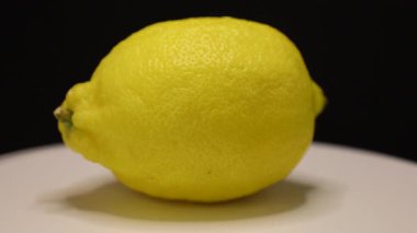 Göz kamaştırıcı bir limon beyaz bir tabakta zarif bir şekilde durur, parlak sarı tonda parlar. Meyve tazelik, yemek tarifleri ve yaz içecekleri için ilham verici fikirler yayar..