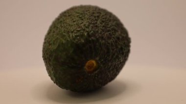 Olgun bir avokado, eşsiz dokusunu ve canlı rengini vurgulayarak ortaya çıkar. Düz bir zemin üzerine kurulmuş bu doğa harikası hayranlığı ve keşfi davet ediyor..