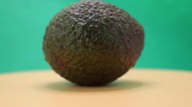 Yumuşak, sarı bir yüzey üzerinde uzanan, parlak yeşil bir zemin üzerinde duran olgun bir avokadonun güzelliğine bakın, eşsiz dokusunu ve rengini sergiliyor. Saf bir sadelik anı.