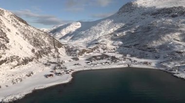 İnsansız hava aracı kıyıdan uzaklaşıyor ve fiyorda doğru uçuyor. Güneş ufka doğru alçalırken uzak dağları ve ılık bir gökyüzünün altındaki karlı kıyı şeridini ortaya çıkarıyor..