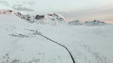 Dron beyaz karı keserek dolambaçlı bir yolun üzerinde ilerler ve Kuzey fiyort bölgesinde sıcak günbatımı ışığı altında çarpıcı bir kontrastlık yaratır..