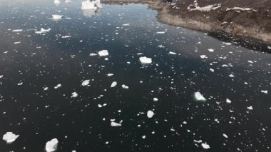 Yukarıdan bakınca Ilulissat, kuru Grönland arazisi ve yansıtıcı suyun yanındaki büyük buzdağını görüyoruz. 