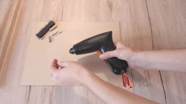 Ellerin biraz bağlanması ve ahşap tezgahtaki siyah elektrikli tornavidayı çalıştırması.. 