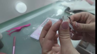 Sahte kirpik kaldırmak için cımbız kullanan ellerin kapatılması, makyaj çalışma alanına çeşitli kozmetik aletler yerleştirilmiş. 