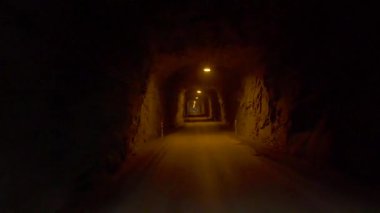 Düz, engebeli bir tünel, doğal kaya geçişleriyle kaplı. Araba ilerlerken, arkasında turuncu ve sarı parlıyor.. 