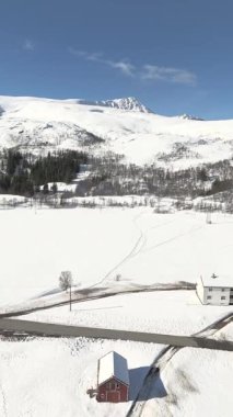 Dikey bir dron kızıl bir evi ortaya çıkarmak için karlı bir dağ yamacından dönerek buzlu sahili ve soğuk kutup denizini ortaya çıkarıyor.. 