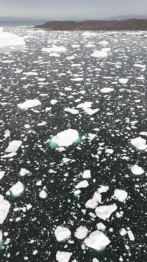 Dikey İHA uzaktaki Grönland kıyı şeridi ve bulutlu Arktik gökyüzü ile sürüklenen buzdağlarının üzerinde ilerliyor..