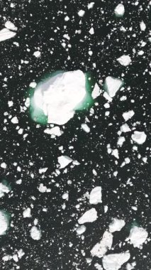 Beyaz buzdağlarının üzerinden aşağıya bakan yavaş dikey drone görüntüsü sakin kutup sularının altındaki sualtı yeşil buzu ortaya çıkarıyor..