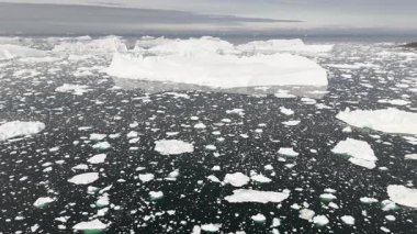 Yatay dron, bulutlu Arktik gökyüzünün altında sonsuz yüzen buzlarla çevrili devasa bir buzdağının yanından geçiyor..