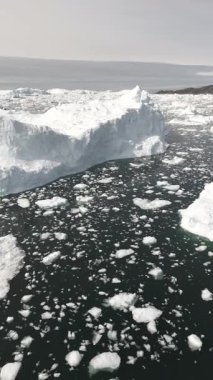Dikey İHA uçuşu, kayan buzlarla çevrili devasa bir buzdağının etrafında dönüyor. Sakin Kuzey Kutbu denizi, yumuşak yaz ışığını yansıtıyor..