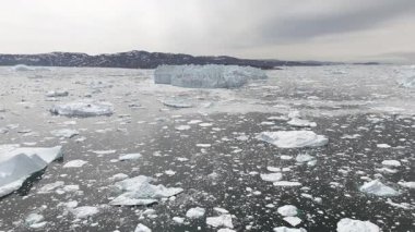 İnsansız hava aracı geriye uçarak genişleyen buz dağları, Grönland kıyı şeridi ve Arktik gökyüzü bulutlarını ortaya çıkarıyor..