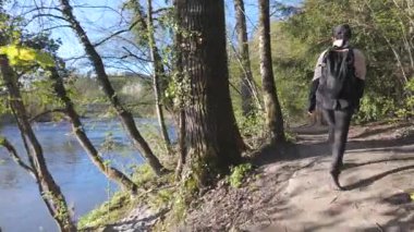 Gün batımının yumuşak ışığı sakin ve aktif bir ruh hali yaratırken bir kadın nehir kenarında yürüyüş yapıyor.