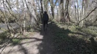 Nehir manzaralı, güçlü bir arka planı ve görünür bir gölgesi olan ağaçlık alanda bisiklet süren ilk kişi.