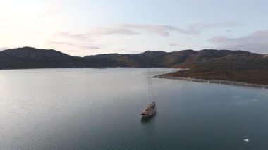 Pürüzsüz dönüş hareketi, kutup deniz manzarası, sürüklenen buz, uzak kara kütlesi, hafif ışık, sakin yaz maceracı ruh haline karşı bir gemi çerçevesi oluşturur.