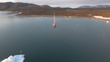 Expansive aerial motion transitions from sea to land, icy waters, barren terrain, muted clouds, calm adventurous feeling in polar summer