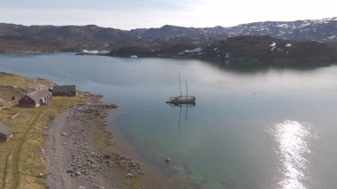 Geriye dönük hava hareketi sahneyi genişletir, tekneler, buzdağları, boş evler, yansıtıcı su ve uzak yaz arazisi ortaya çıkar.