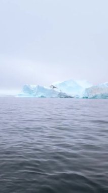 Büyük donmuş oluşumlar soğuk kuzey sularında sürükleniyor, sislerin arasından yükselen mavimsi tonlar, Ilulissat 'ta sessiz ve düşünceli bir hava yaratıyor.