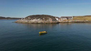 Grönland 'daki bir fiyordun sakin ve soğuk sularında sürüklenen küçük sarı bir teknenin havadan görünüşü.