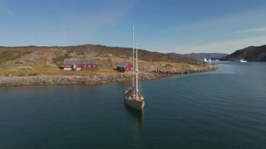 Grönland 'ın arka planında buzdağları olan sakin bir koyda demirlemiş bir yelkenlinin hava görüntüsü.