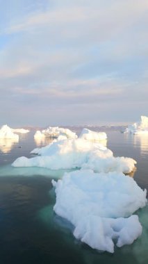 Grönland 'ın soğuk okyanus sularında sürüklenen devasa buzdağları manzaralı bir günbatımında
