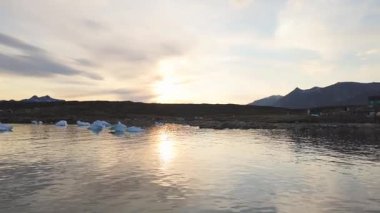 Gece yarısı güneşi, Grönland, Saqaq kıyılarında yüzen buzdağlarıyla sakin denizi yansıtıyor.