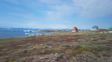 Okyanusta yüzen devasa buzdağlarıyla Saqqaq kıyı yerleşiminin havadan görüntüsü.