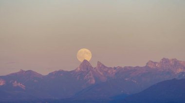 Karlı Dents ve Oche dağlarının zirvelerinde alacakaranlık gökyüzünde yükselen görkemli dolunay.