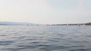 İsviçre 'deki Cenevre Gölü' nün sakin su yüzeyinde güneşli bir yaz gününde yelkenliler geziniyor.