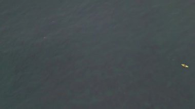 Sakin, derin mavi bir denizde tek başına kano süren bir insanın yukarıdan aşağıya bakan görüntüsü.