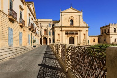 Noto, Sicilya, İtalya 'daki barok mimari ve antik binaların güneşli sabah manzarası. Gölgeleri ve süslü balkonları olan tarihi bir cadde..