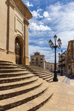 Enna, Sicilya, İtalya 'da tarihi bir meydanın güneşli manzarası. Antik taş binalar, açık kafe masaları ve klasik sokak lambaları büyüleyici bir Akdeniz atmosferi yaratır..