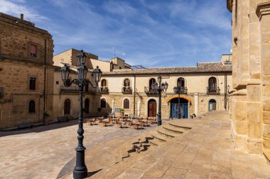 Enna, Sicilya, İtalya 'da tarihi bir meydanın güneşli manzarası. Antik taş binalar, açık kafe masaları ve klasik sokak lambaları büyüleyici bir Akdeniz atmosferi yaratır..