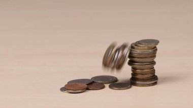 Yığılmış bozuk paraların statik görüntüsü yere düşüp ahşap bir masanın üzerine düşüyor ve dağınık bir yığın oluşturuyor. Mali dengesizlik, harcamalar, kayıp, tasarruf riski ve para yönetimi kavramı. En az bir çekim stüdyo videosu.