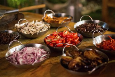 İçinde kiraz domatesleri, kırmızı soğan, mantar, zeytin ve metal kaselerde servis edilen kavrulmuş biberlerin de bulunduğu taze sebze soslu Akdeniz antipasti büfesi. Yemek ve restoran yemek gösterisi konsepti.