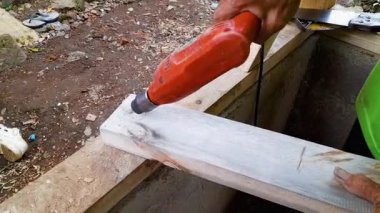 Marangoz elektrikli elektrikli aletle tahta döşemede delik açıyor. İnşaat işçisi yenileme projesi için kırmızı matkap kullanıyor. Kereste marangozluğu işi için el tutma ekipmanı.