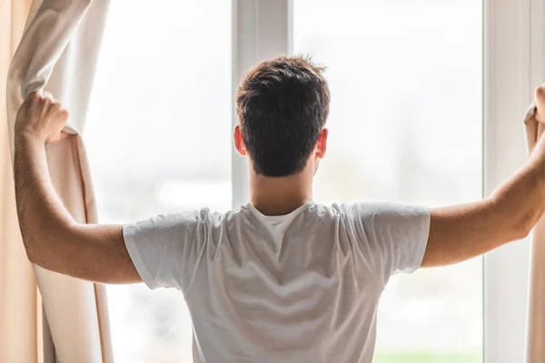 Foto av medelålders man öppna gardiner i hotellrum på morgonen. — Stockfoto