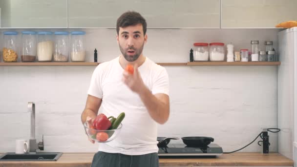 4k-Video eines fröhlichen jungen Mannes, der Gemüse jongliert, während er in der Küche Essen zubereitet. — Stockvideo