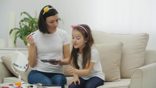 4k video von mutter und sie süß tochter doing make up zusammen sitzen auf weiß couch. — Stockvideo