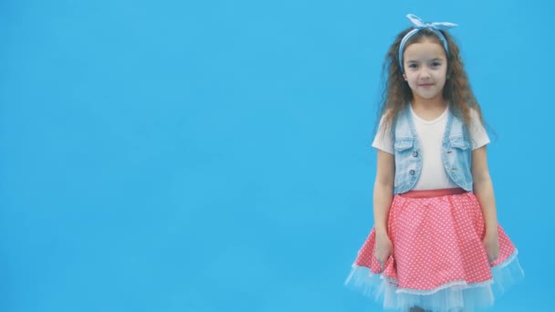 LIttle menina de pé sobre fundo azul em 4k slow motion vídeo. — Vídeo de Stock