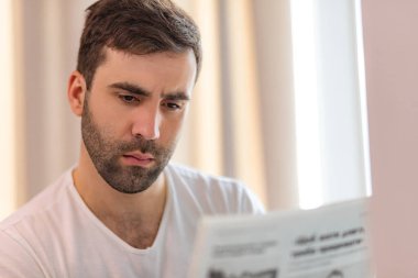 Evdeki kanepede oturmuş gazete okuyan genç adamın fotoğrafı..