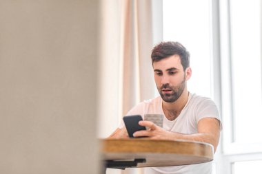 Yakışıklı bir gencin evdeki kanepede otururken akıllı telefonunu kullanmasının fotoğrafı..