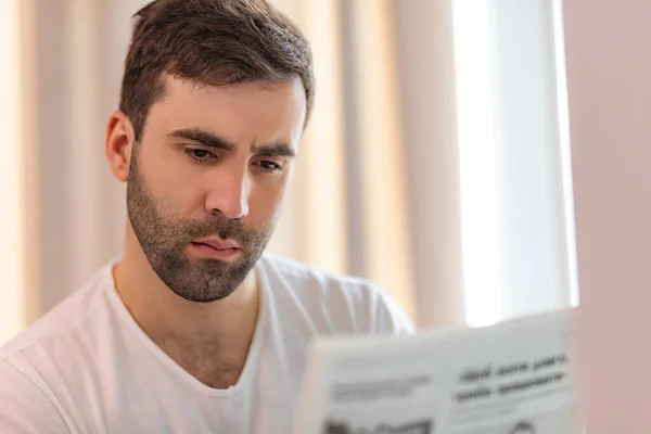 Foto av ung man sitter på soffan läsa tidningen hemma. — Stockfoto