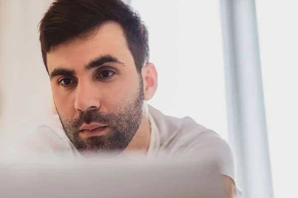 Beskuren bild av ung man tittar och arbetar på datorn laptop hemma. — Stockfoto